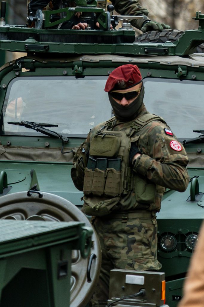 A Polish soldier in uniform stands in front of a military vehicle in Kraków.